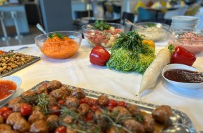 Ein Buffettisch mit verschiedenen Salaten, frischem Gemüse, Soßen, einem Teller mit gekochten Fleischbällchen mit Kirschtomaten und einer Schüssel mit geraspelten Möhren.